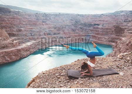 Young sporty girl wearing blue activewear stretching outdoors. Woman training yoga pose on mountain hill, calm and silent view.