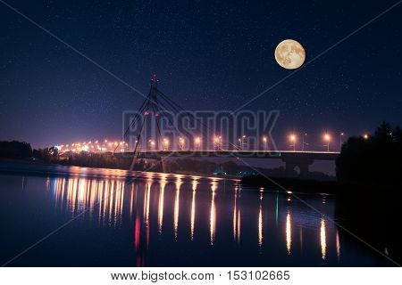 Moscow bridge in Kiev at night with colorful illumination and reflection in Dnieper river and big moon