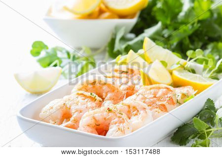 Seafood. Shrimps prawns with fresh herbs and lemon on white plate on wooden white background
