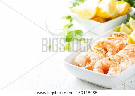 Seafood. Shrimps prawns with fresh herbs and lemon on white plate on wooden white background