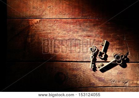 Three vintage keys on old wooden background under beam of light