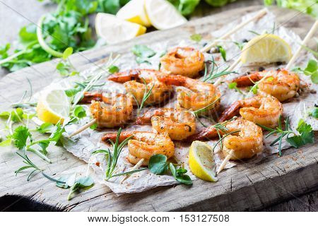 Seafood. Shelfish. Grilled fried Shrimps Prawns on wooden skewers with spices and fresh herbs on wooden rustic cutting table on wooden background. Srimps prawns brochette kebab. Barbecue srimp
