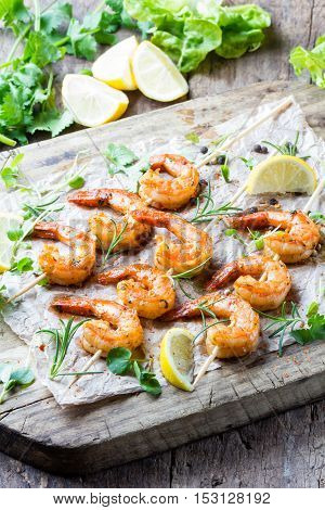 Seafood. Shelfish. Grilled fried Shrimps Prawns on wooden skewers with spices and fresh herbs on wooden rustic cutting table on wooden background. Srimps prawns brochette kebab. Barbecue srimp
