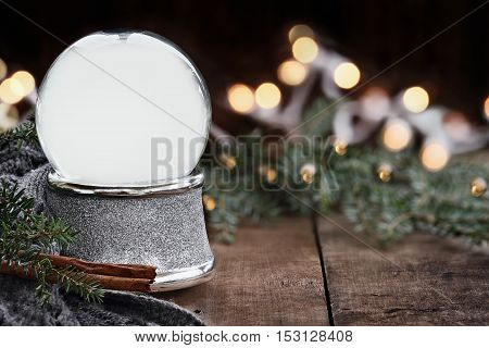 Rustic image of an empty snow globe surrounded by pine branches cinnamon sticks and a warm gray scarf. Shallow depth of field with selective focus on snowglobe.