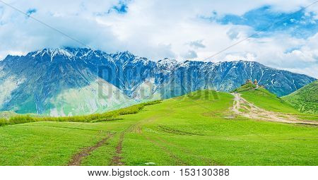 The long way through the green highland meadows to the medieval Gergeti Trinity Church at the foot of Kazbek Mount Kazbegi National Park Georgia.