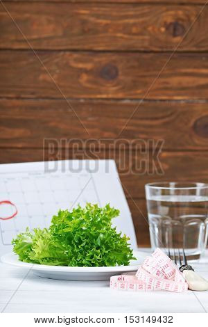 Diet concept. Fresh salat, water and measurement tape - diet and healthy eating concept. Starting new life from monday. On a wooden background