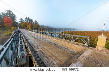 Early October, misty morning sunshine on a portable deployable, single lane, steel and timber bridge over Corry Lake in Chalk River Ontario, Canada.