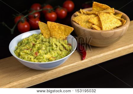 Guacamole in white bowl on natural wooden desk with tortilla chips.