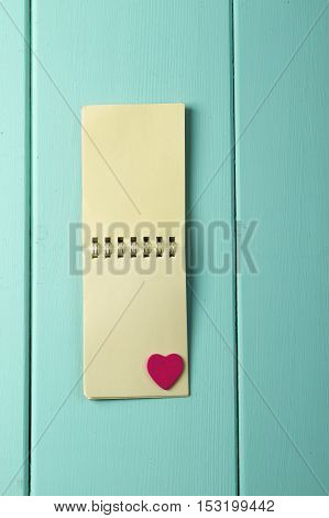 wooden red heart and a notebook on a spring on a wooden turquoise background. vertical shot. love notes