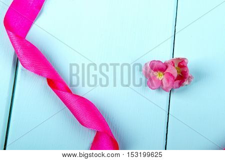 wooden background turquoise satin ribbon and pink begonia flower.