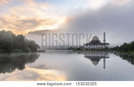 View and reflection of Darul Quran Mosque with fogs and stunning clouds during sunrise.