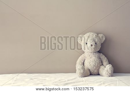 vintage teddy bear sit on the right side white bed at headboard and brown flat wall background for gift and surprise