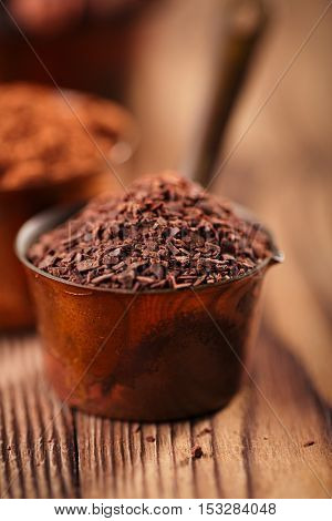 grated chocolate, powder and cocoa beans in vintage measuring copper pans  on old wooden background