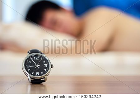 close-up at wristwatch and clock face show the time around 9 o'clock with background of blur man sleeping on the bed wake up late hurry to work or hangover from last night