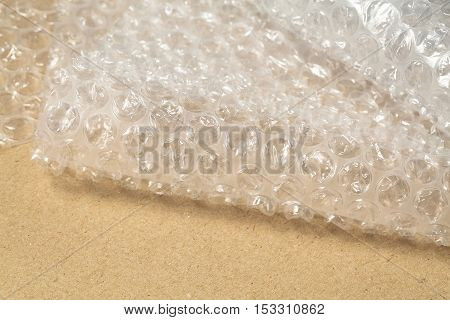 Protective bubble wrap on cardboard texture background. Packaging materials concept, close up.