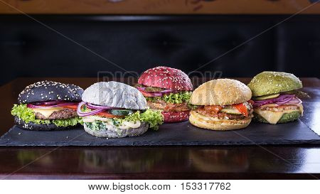 Assorted colored burgers with different fillings with sesame seeds on slate blackboard