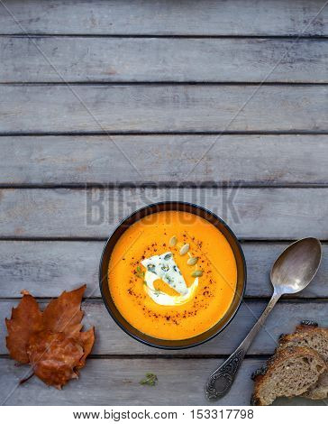 Hot pumpkin soup with blue cheese, herbs and multi-cereal bread on a wooden table with your text on top. View from above