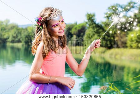 Conceptual beauty portrait of little girl dressed up as little princess. Girl casting spell with magic wand next to lake.