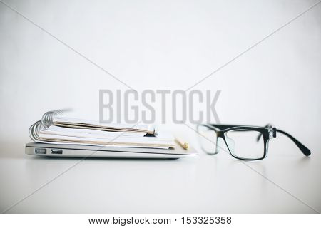 Close up of eyeglasses closed laptop and notepads on bright desktop