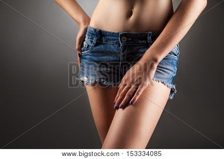 Slim girl with naked navel in denim shorts posing faceless. Studio portrait black background.