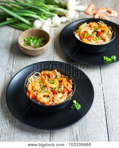 Noodles with bean sprouts and shrimp in black bowls.