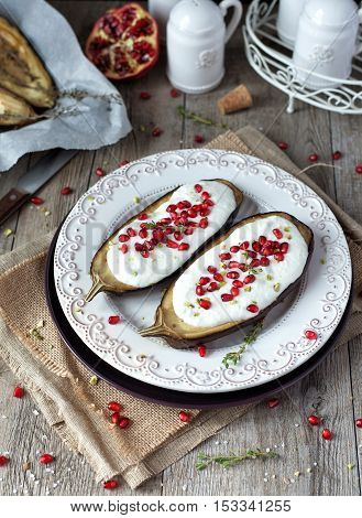 Roasted eggplants with yogurt sauce and pomegranate seeds on a rustic table.