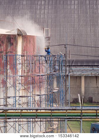 Worker cleaning storage tank by air pressure sand blasting in high position.