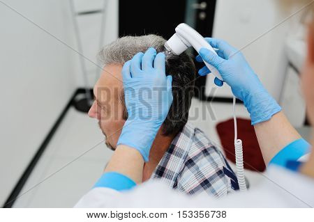 baldness. diagnostics hair and scalp. Trihoskopiya. Doctor examine patient male hair a special apparatus.