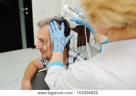 baldness. diagnostics hair and scalp. Trihoskopiya. Doctor examine patient male hair a special apparatus.