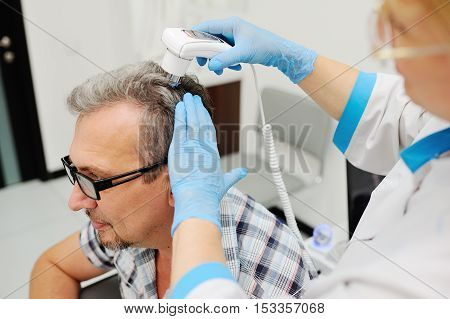 baldness. diagnostics hair and scalp. Trihoskopiya. Doctor examine patient male hair a special apparatus.