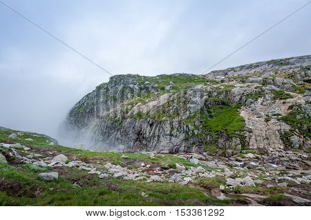 Tourists at the scenic landscape of Kjerag hiking path at cloudy and foggy weather. Lysefjord, Norway.