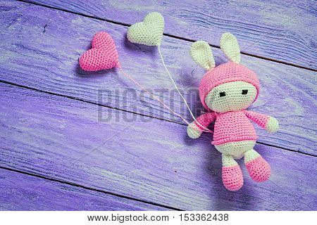 Handmade crochet rabbit toy with heart shape baloons on wooden background. Amigurumi doll space for text