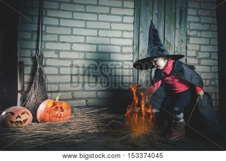 Little baby witch making a magic potion at Halloween night. Horror. Pumpkins, broom. Halloween costumes for child. Witch.