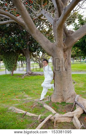 Young boy with white sailor suit leaning on a big tree in his First Communion