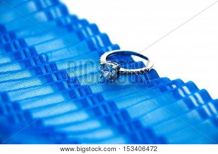 Silver ring with cubic zirconia rests on a blue corrugated tape