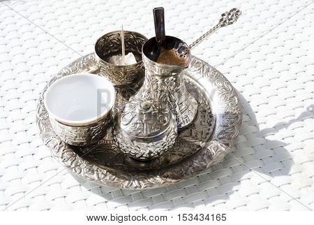 A metallic tray with copper plated cezve (džezva) filled with traditional foam Bosnian coffee a silver pot with turkish delight rahat lokum a clay cup and sugar cube pot served in an ornament Sarajevo set.