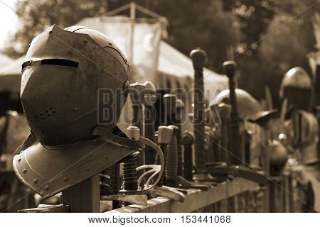 Old medival weapons and some helmets, stacked in a row.
