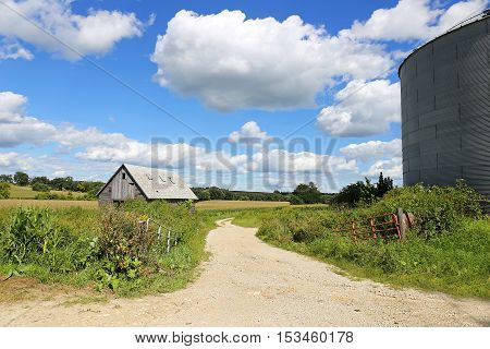 A beautful landscape scenery of rolling country hills and fields and blue cloudy sky with an old wooden farm barn or shed and a steel grain storage bin.