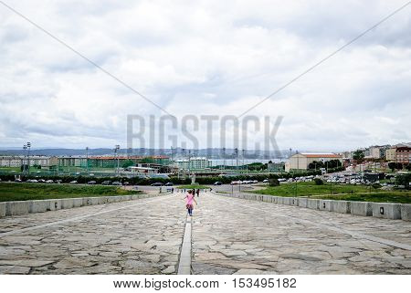 La Coruna Spain - May 28 2016: People walking on promenade towards Hercules tower Torre de Hercules roman lighthouse UNESCO world heritage Coruna Galicia Spain.