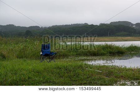 Abandoned blue camping chair on the lake shore surround by grass and reeds