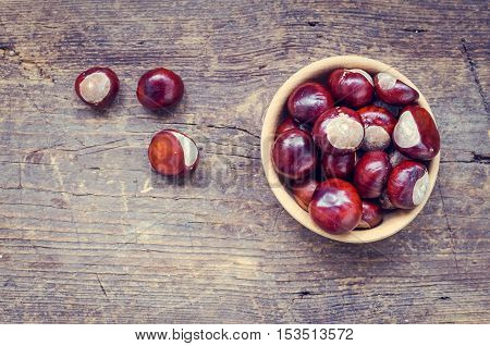 Fresh chestnuts in a bowl on an old wooden table. Group of chestnuts. Chestnuts - fruits horse chestnut - Aesculus hippocastanum. Dark background. Autumn background. Top view. Copy space.