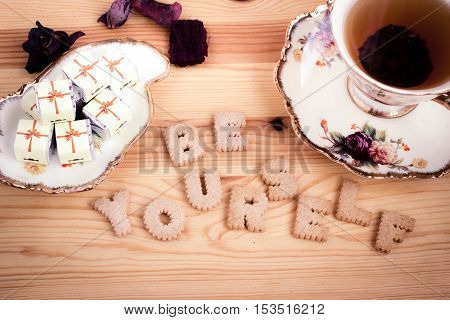 Be Yourself, inspirational slogan made from biscuit letters with chocolate sweets and a cup of tea on wooden background. Toned image.