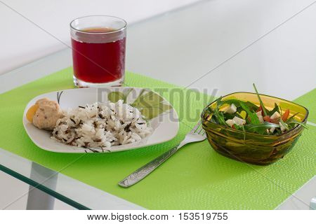 Boiled parboiled wild rice with chicken meatball and salad with arugula, tomatoes and feta cheese. Cherry juice in glass. Colorful dinner on glass table.