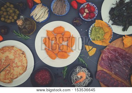 Table with plates of spanish tapas - jamon, croquetes, guacamole and olives, top view, picnic table, retro toned