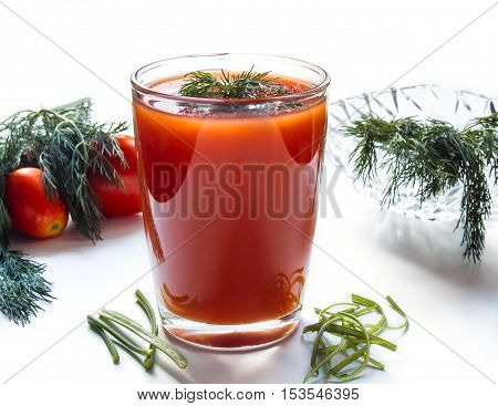 Tomato juice in a tall glass on a white background with herbs and tomatoes