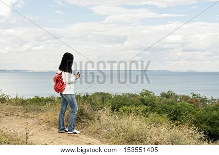 Young girl (brunette) and jeans with a red backpack looking out to the sea. Selective focus.