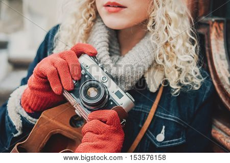 Old film camera in the hands of a young blond curly female in warm red gloves winter