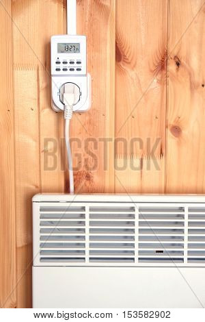 Working white electric convector heater plugged to timer power socket operated in smart house system against wooden wall inside room front view closeup