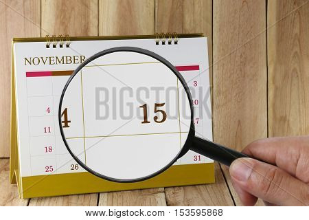 Magnifying glass in hand on calendar focus you can look number 15 in November Concept in business and meetings.