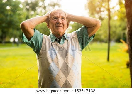 Man holding head in despair. Elderly guy outdoor. Burden of mistakes. Horrible things have happened.